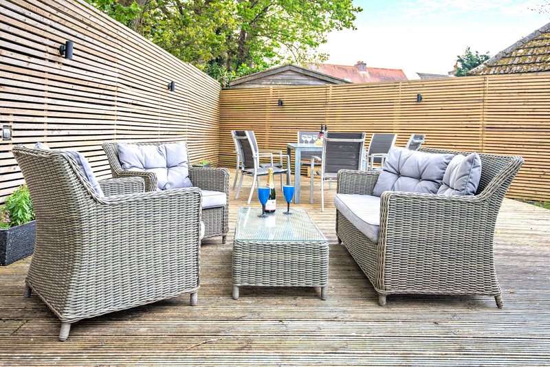 Outdoor patio with rattan furniture, cushions, blue bottles and wooden decking