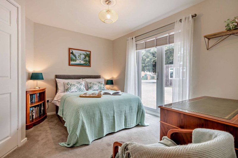 Bright bedroom with double bed, wood furniture, armchair, and patio doors to garden