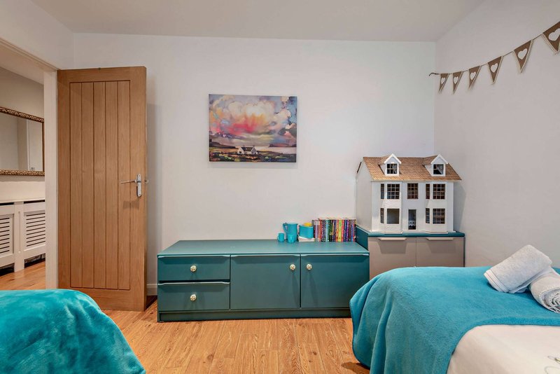 Shared bedroom with two single beds, teal storage chest, wooden door and hardwood flooring