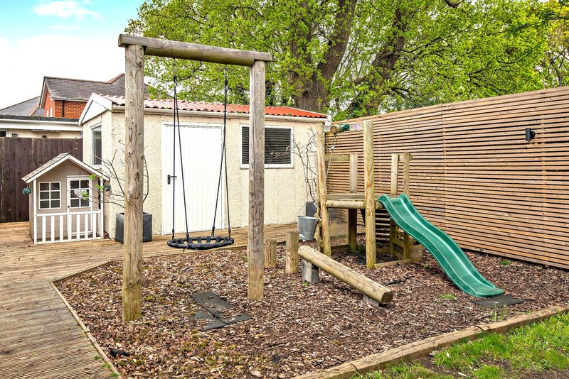 Backyard play area with wooden swing set, slide, and small playhouse structure