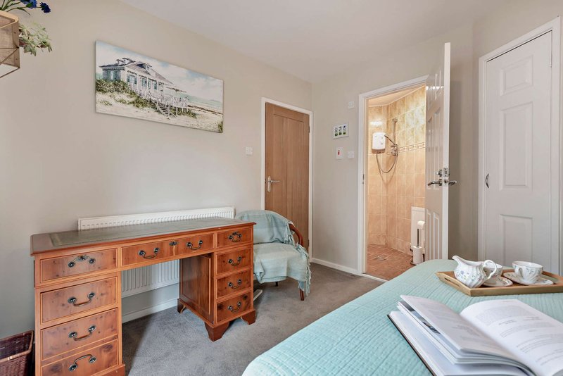 Bedroom with double bed, wooden desk, open bathroom door and framed landscape artwork