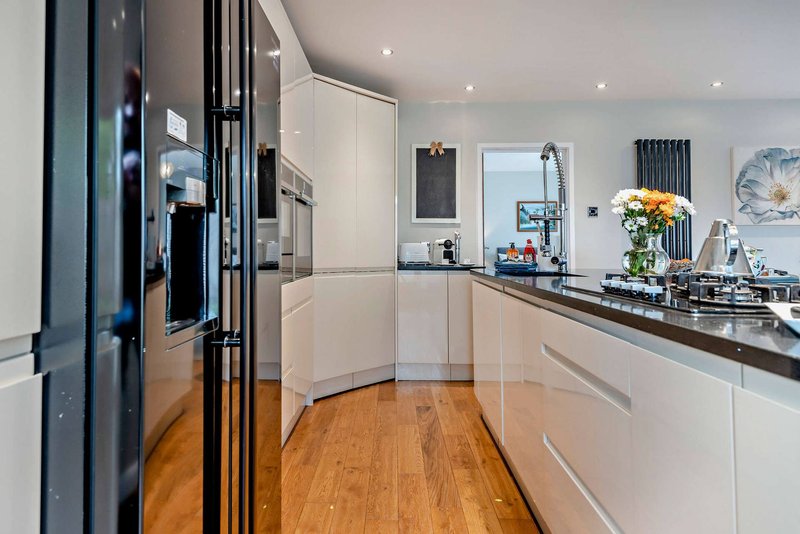 Modern kitchen with white cabinetry, black countertops, wooden flooring and stainless steel appliances