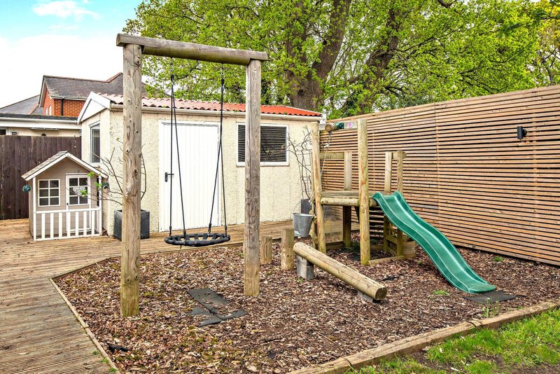Backyard play area with wooden swing frame, slide, and small playhouse