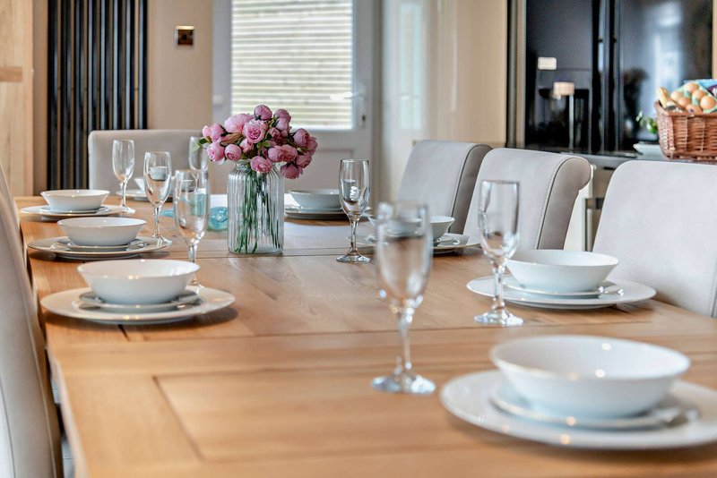 Dining room with wooden table set for meal, pink flowers, place settings and glassware