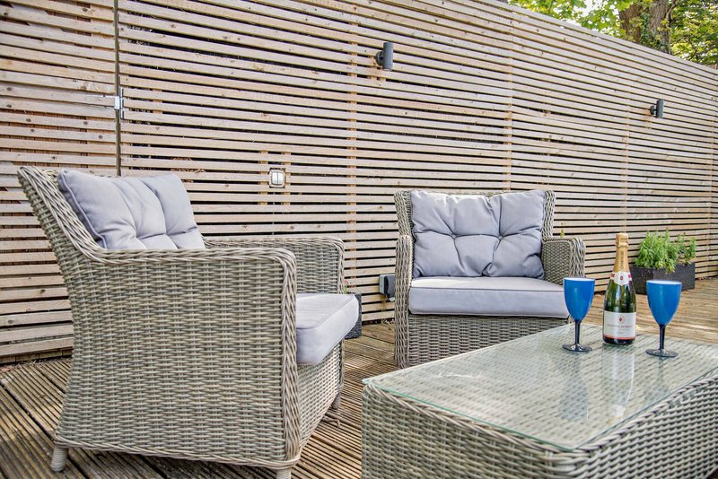 Outdoor patio with wicker furniture, cushions, wooden decking and slatted fence backdrop