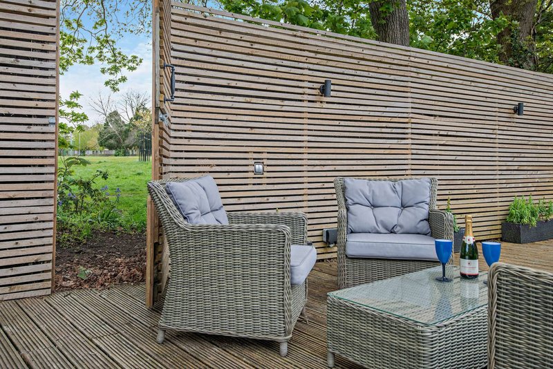 Outdoor deck with wicker seating, cushions, small table and garden views