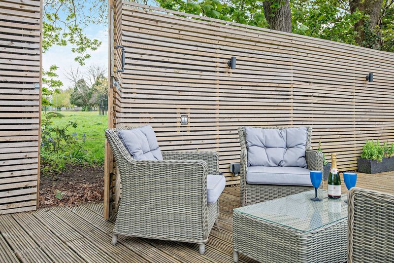 Outdoor decking area with wicker seating, cushions, table and garden views