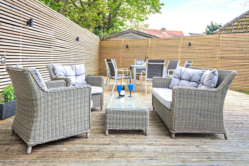 Outdoor patio with rattan furniture, cushions, wooden decking and garden fence