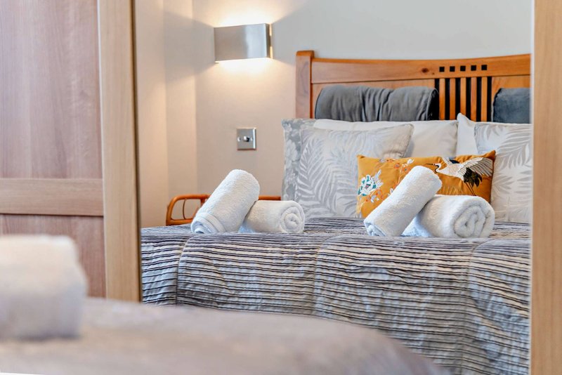 Bedroom with wooden bed frame, striped bedding, rolled towels, and decorative pillows