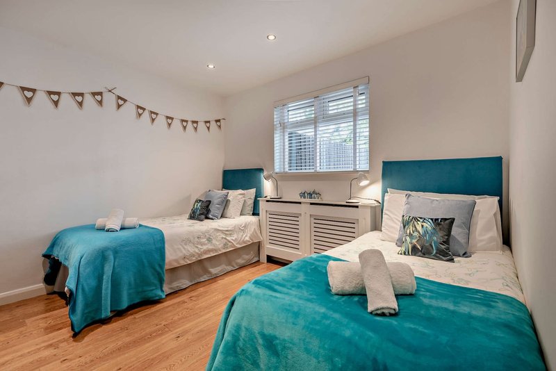 Bright twin bedroom with teal headboards, white bedding, wooden floor and window