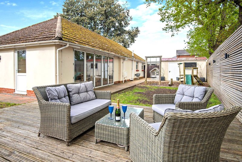 Outdoor patio with rattan furniture, cushions, and garden view from property