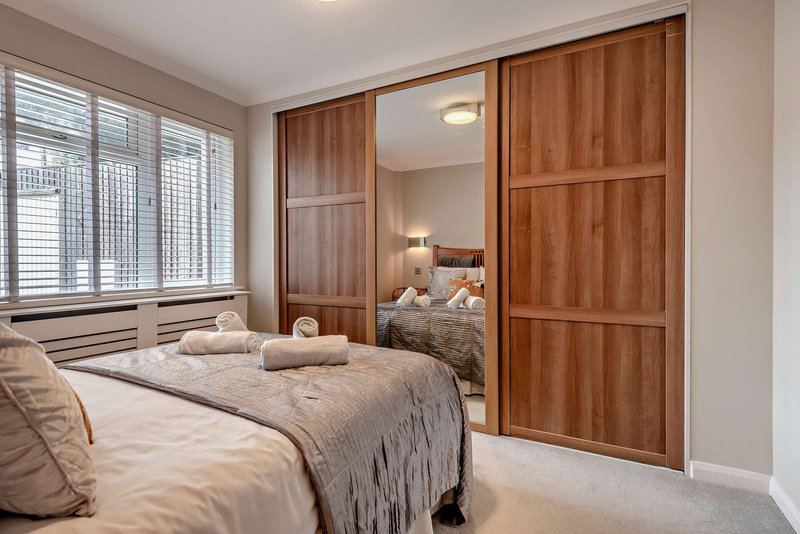 Modern bedroom with double bed, wooden wardrobe doors, and large windows with blinds
