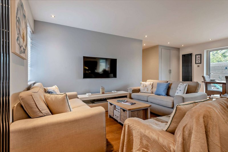 Modern living room with tan sofas, wall-mounted TV, wooden coffee table and natural light from windows