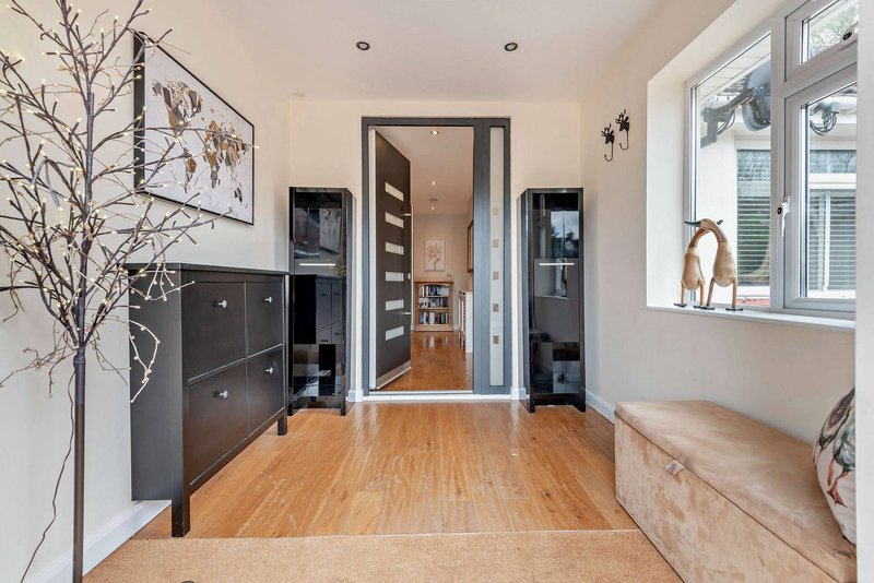 Modern hallway with wooden flooring, dark furniture, framed wall art, and bright windows
