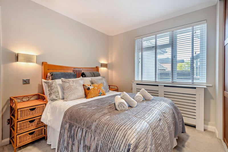 Bright bedroom with wooden bed frame, neutral bedding, wooden nightstand and shuttered window