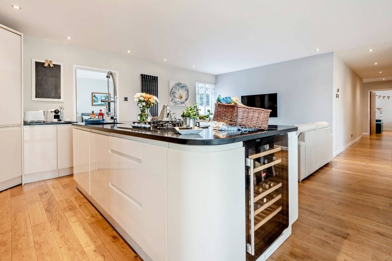 Modern open-plan kitchen with white cabinetry, black countertop, island with wine fridge, and wooden flooring
