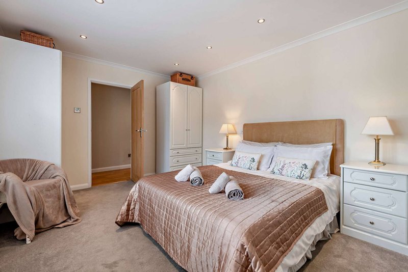 Spacious bedroom with double bed, wooden headboard, bedside tables, wardrobe and armchair