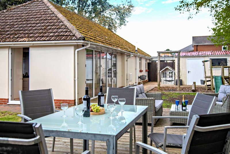 Outdoor patio area with dining table, chairs, and bottles beside cottage buildings