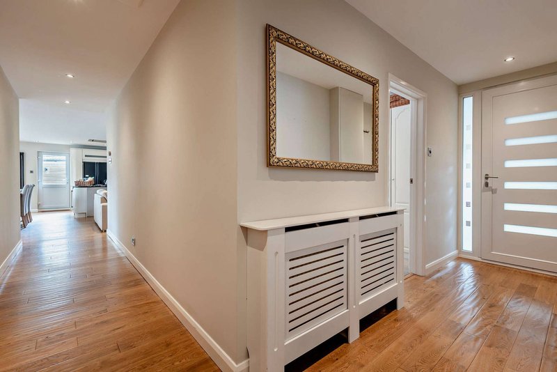Bright hallway with wooden floor, white cabinetry, framed mirror, and modern interior doors