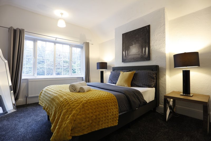Comfortable double bedroom with a spacious bed, ample natural light and a large window overlooking the outside greenery — a quiet, relaxing space for a good night’s sleep after work.