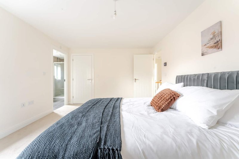 Bright bedroom with double bed, blue headboard, white bedding and orange cushion