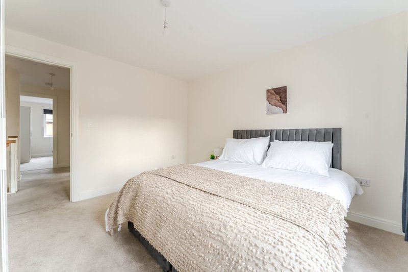 Bright bedroom with double bed, grey headboard, beige bedding, and open doorway