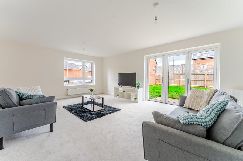 Bright modern living room with gray sofas, TV unit, black rug and garden views