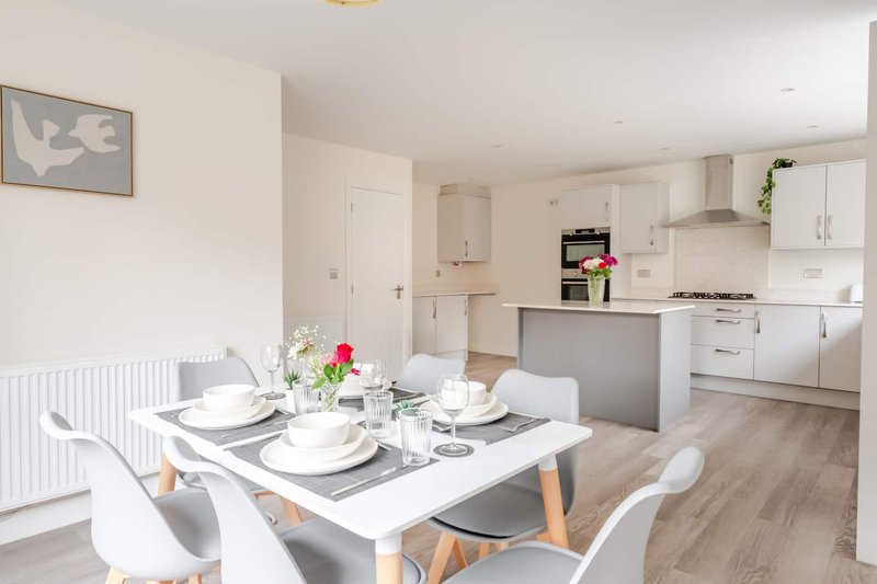 Open-plan kitchen and dining area with white table, chairs, and modern cabinetry