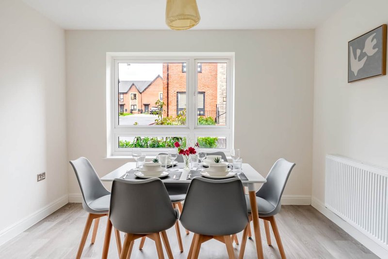 Dining room with black table, grey chairs, window overlooking street and brick houses