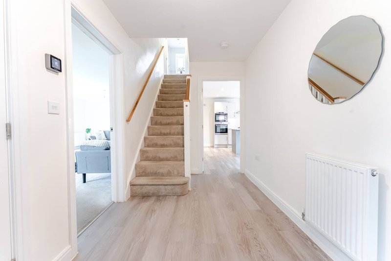 Bright hallway with wooden flooring, stairs, round mirror and white walls