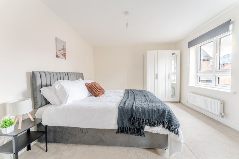 Modern bedroom with grey upholstered bed, white bedding, and large window overlooking street