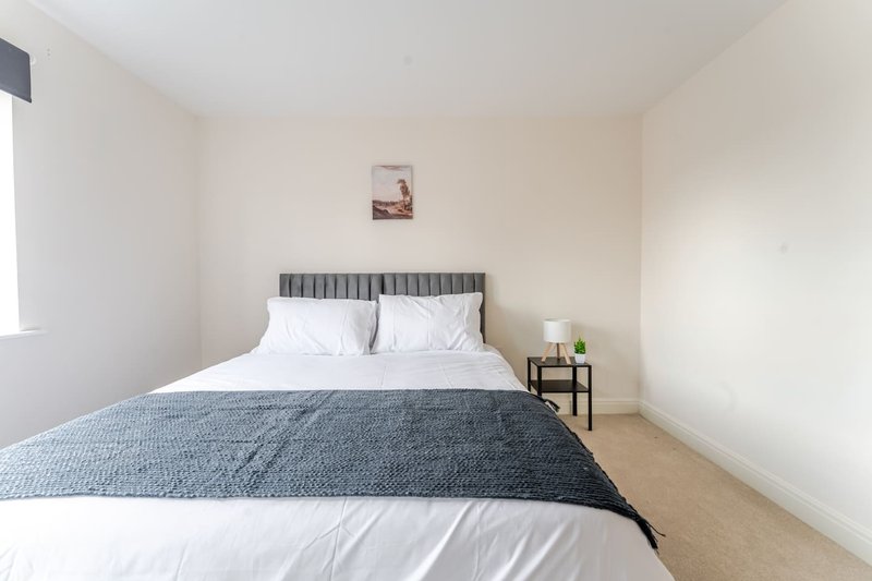 Bedroom with double bed, grey headboard, white pillows, blue bedding, and bedside table