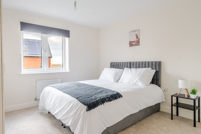 Bright bedroom with gray upholstered bed, white bedding, and window with orange-framed exterior view
