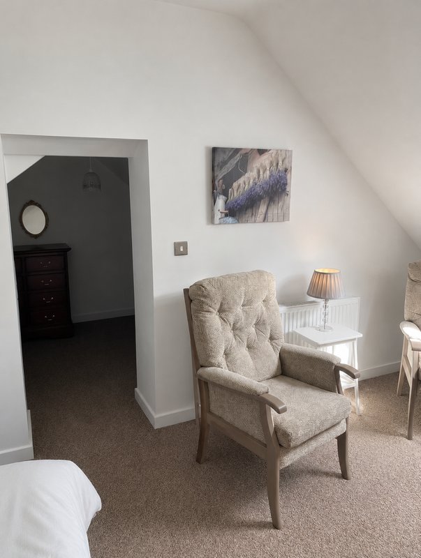 Attic bedroom with beige armchair, side table, lamp, and doorway to ensuite