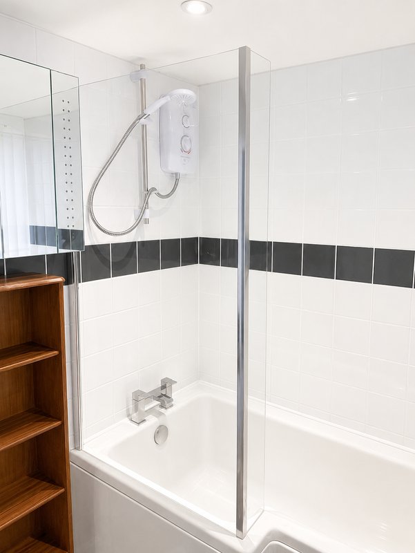 Modern bathroom with white subway tiles, black accent stripe, glass shower enclosure and wooden storage unit