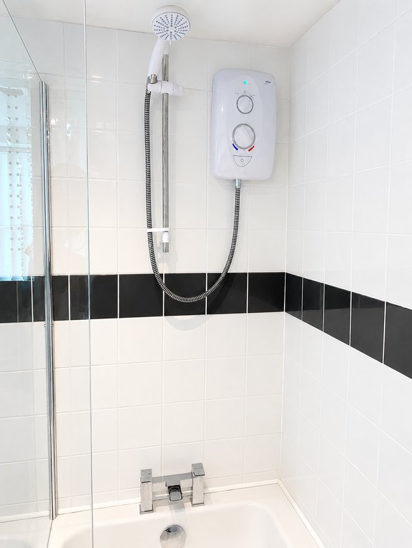 Modern bathroom shower enclosure with white tiles, black accent strip, and electric water heater