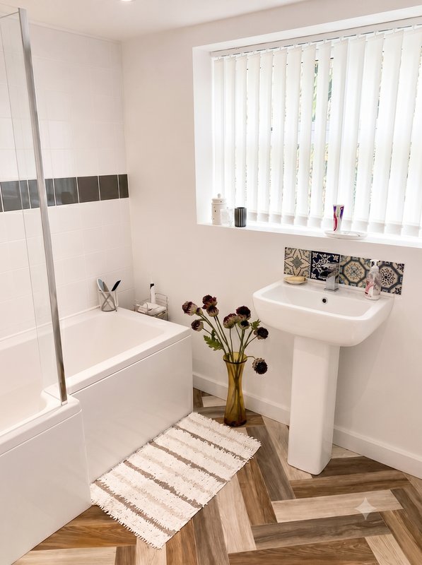 Modern bathroom with white bath, pedestal sink, shower enclosure and wooden flooring