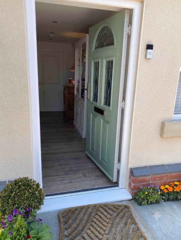 Open green front door showing hallway and kitchen beyond, with potted flowers outside