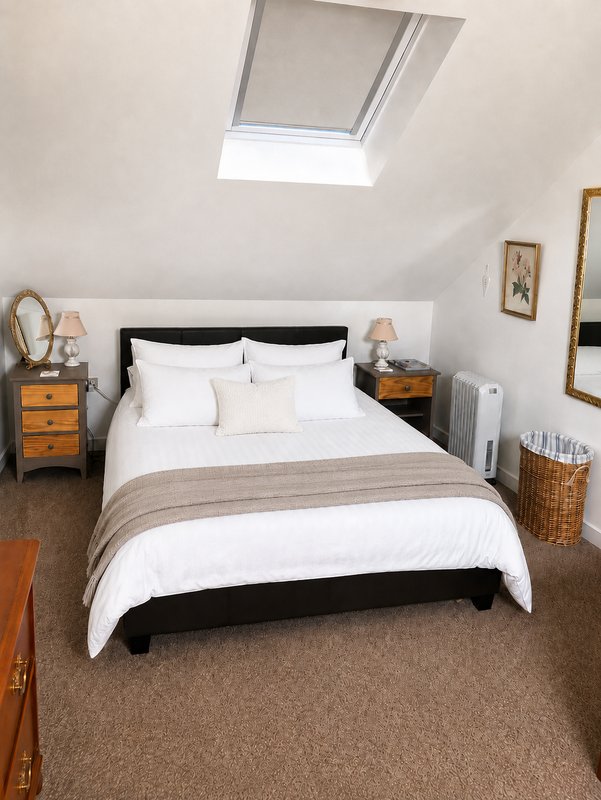 Attic bedroom with double bed, skylight, wooden nightstands, and neutral décor