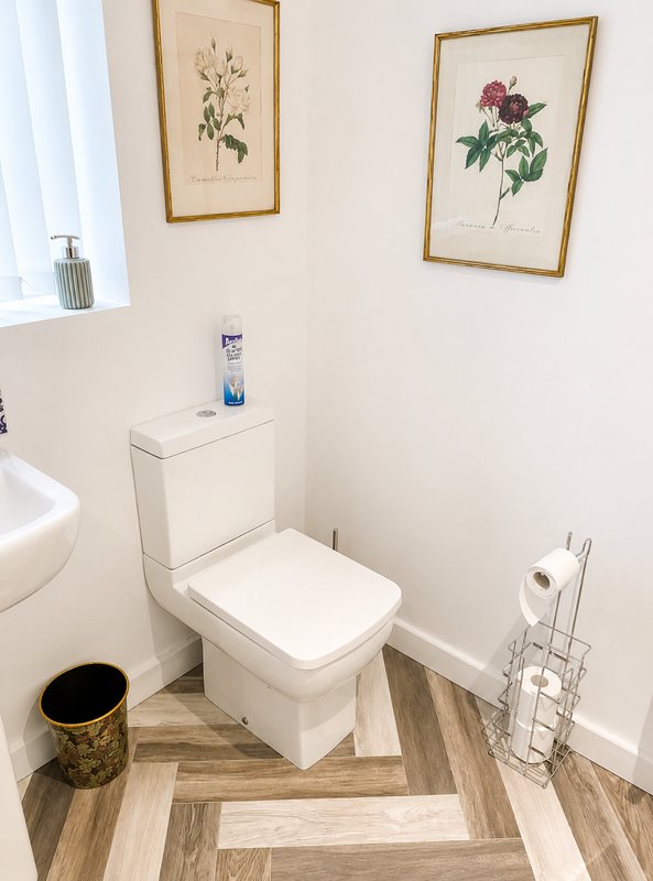 Clean bathroom with white toilet, botanical wall art, herringbone wood-effect flooring