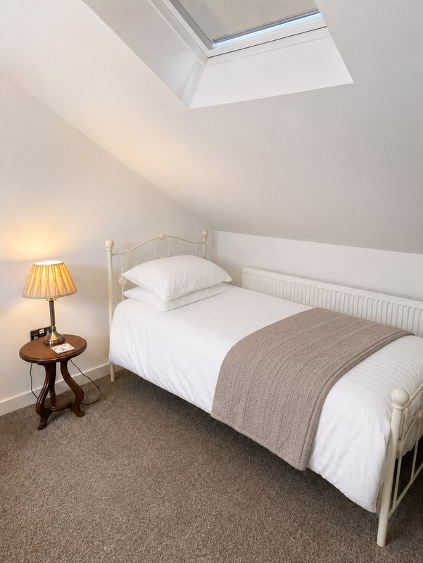 Bright attic bedroom with single bed, white bedding, wooden side table and skylight window