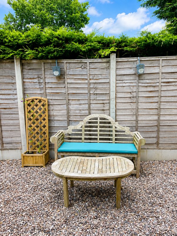 Garden patio area with wooden bench, round table, trellis and fence backdrop