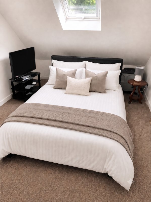 Attic bedroom with double bed, neutral bedding, black headboard and nightstands, skylight window