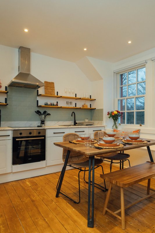 Modern kitchen with white cabinetry, wooden dining table and chairs, large window view