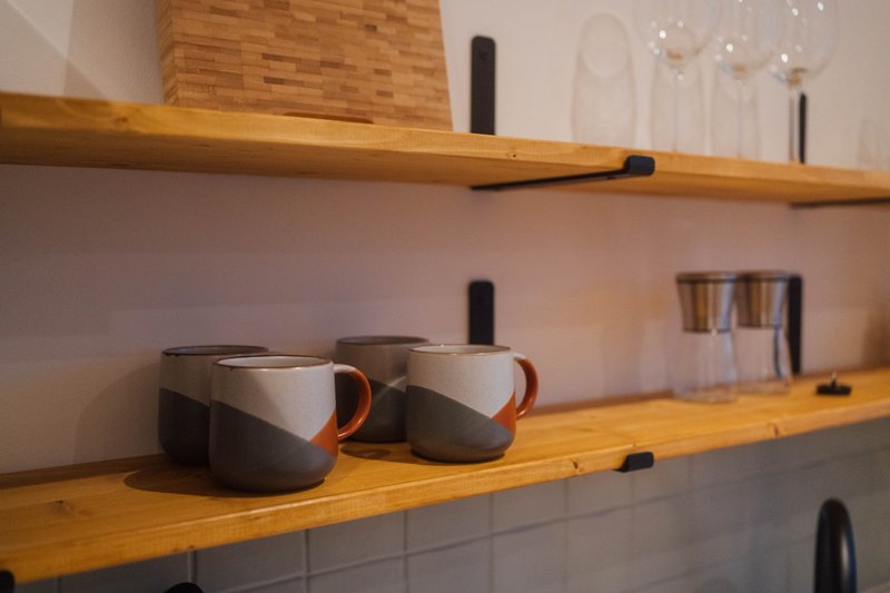 Wooden open shelving with two ceramic mugs and glassware, white subway tile backsplash