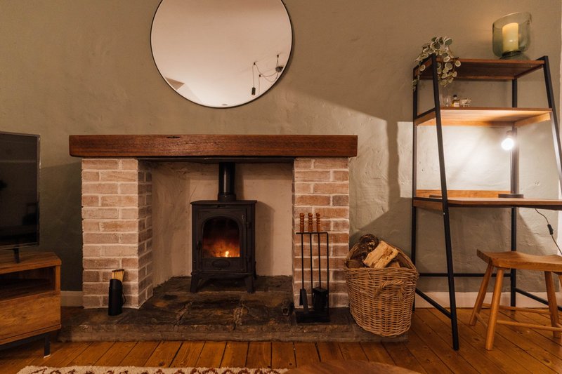 Living room with brick fireplace, wood-burning stove, round mirror, and wooden furniture