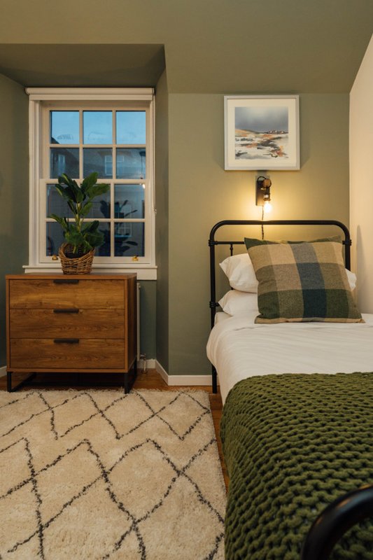 Bedroom with metal bed frame, wooden dresser, window, potted plant and framed artwork