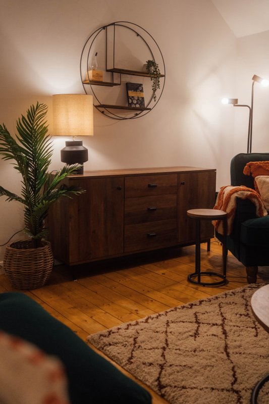 Living room with wooden dresser, round wall shelf, table lamp, potted plant and armchair