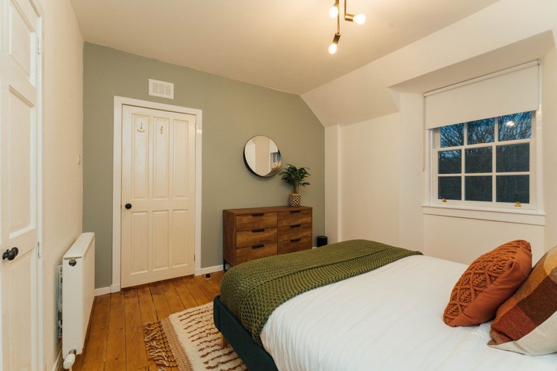 Bright bedroom with double bed, wooden dresser, green accent wall, and window with night view