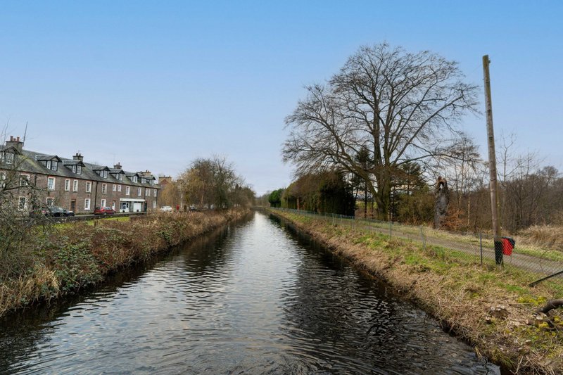 Canal with bare trees, brick building on left, open grassland and utility pole on right